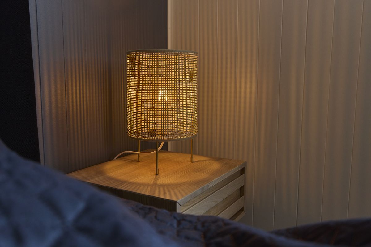 Woven bedside lamp casting warm light on a wooden wall