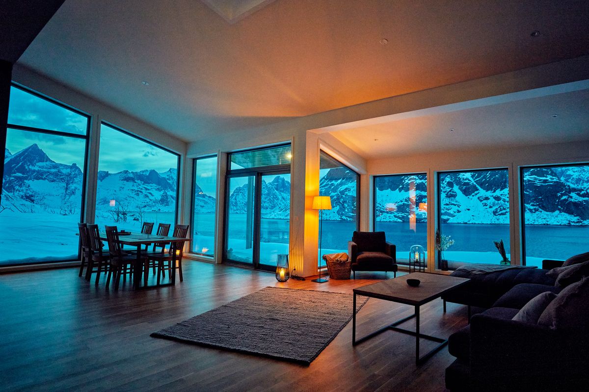 Dining table and sofa in Reine at blue hour with panoramic windows onto the mountains