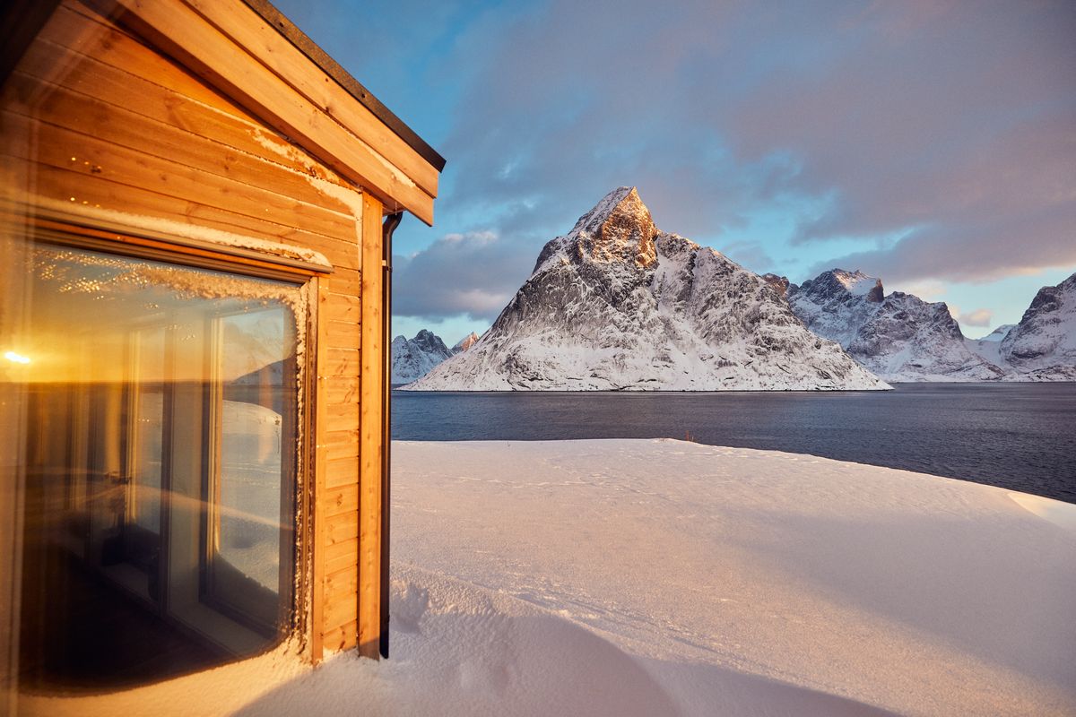 Glass corner of the Reine house, warm light inside and a snowy peak outside