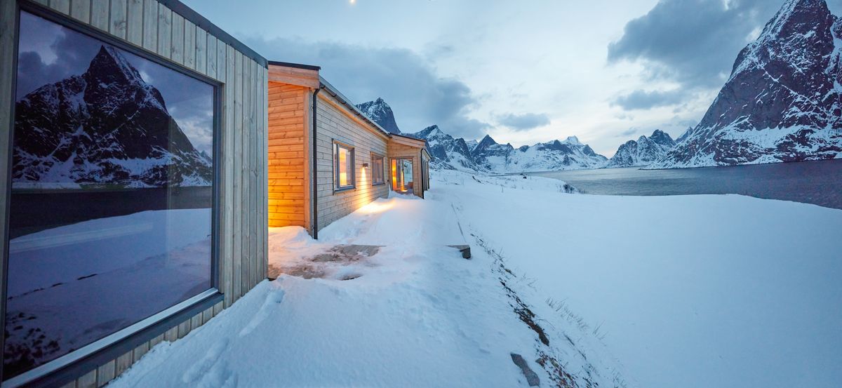 Panorama of the Reine house in winter, its glass front reflecting the last light on the mountains