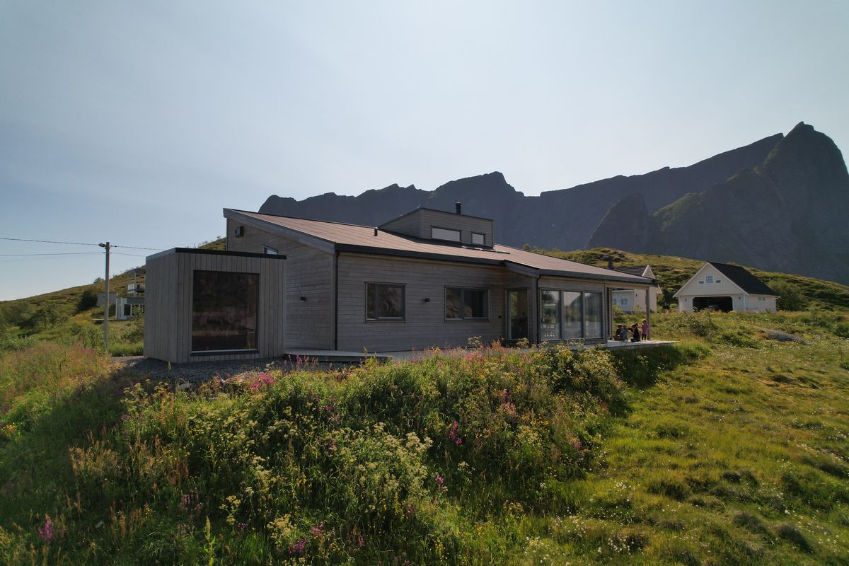 The Reine house in summer on a green slope, mountains behind