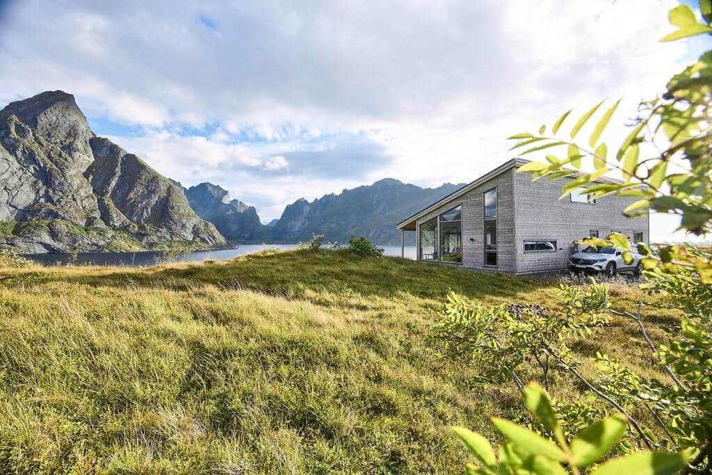 The Reine house in summer, green meadow in front and steep mountains across the fjord