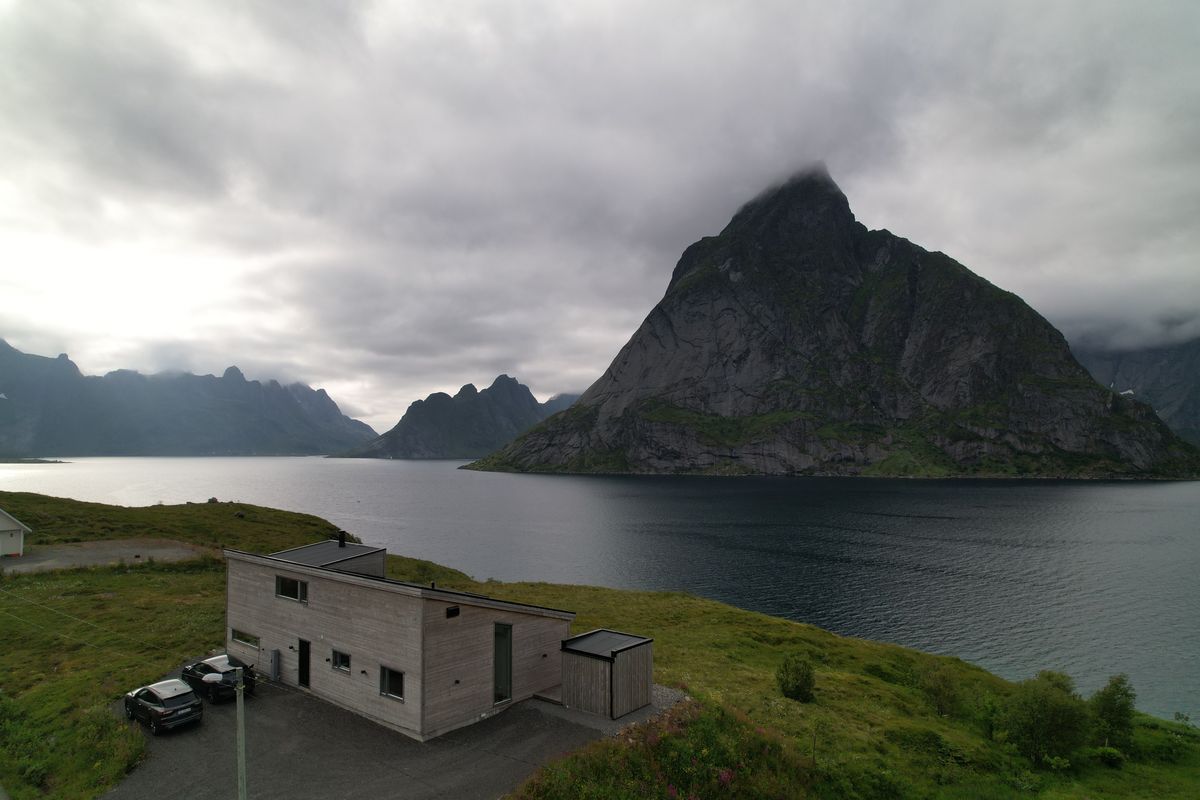 The Reine house in summer by the fjord, a steep peak under low clouds