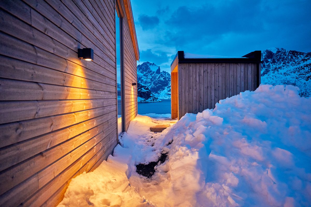 Dark wooden facade of the Reine house with snow piled up against the wall