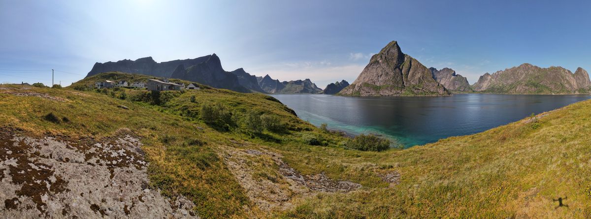 Summer panorama near Reine: green slopes, a lake and sharp peaks under a blue sky